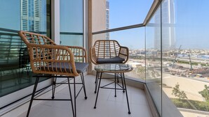 Ein Balkon mit Korbstühlen und einem Glastisch, der einen Blick auf die Stadt und hohe Gebäude bietet.