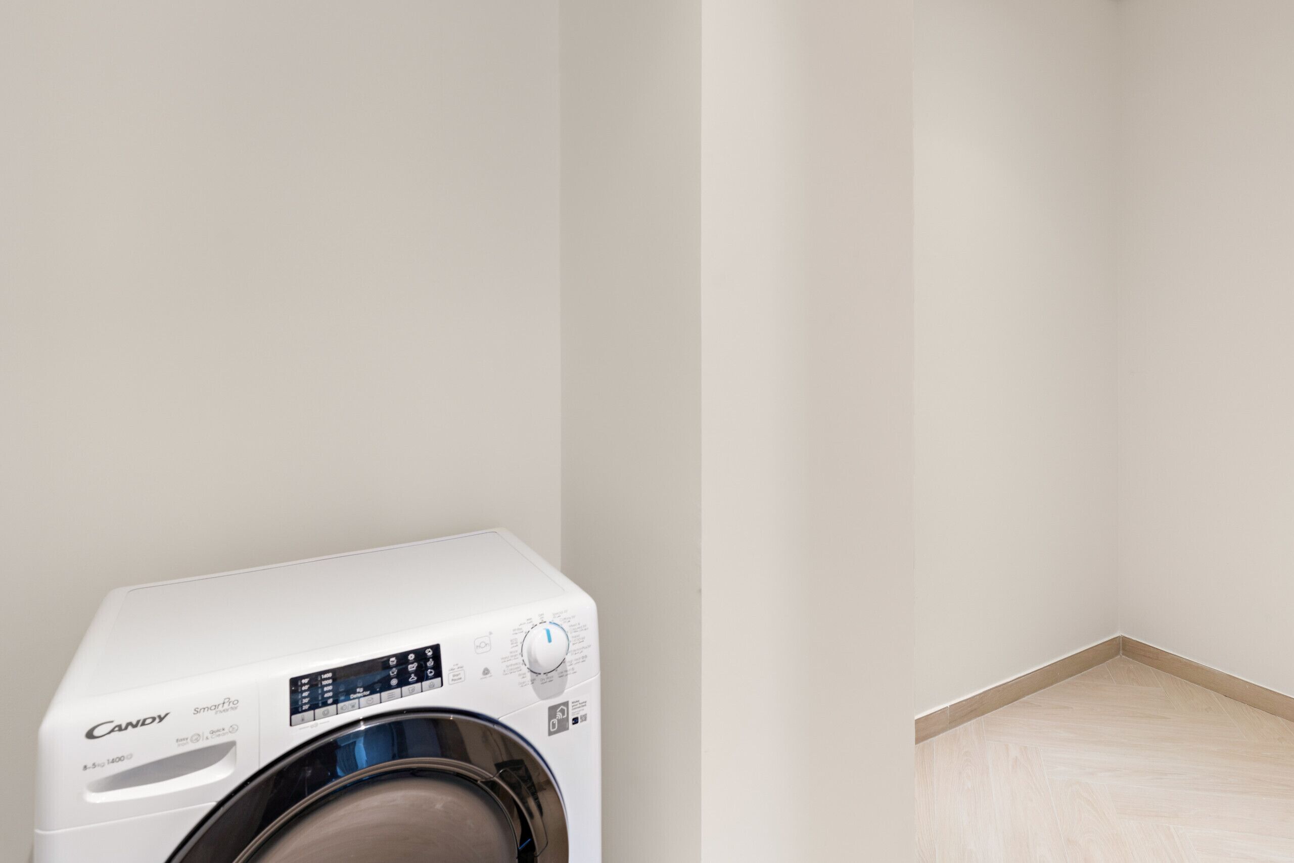 A white Candy SmartWash washer in a corner of a room with a wooden floor.