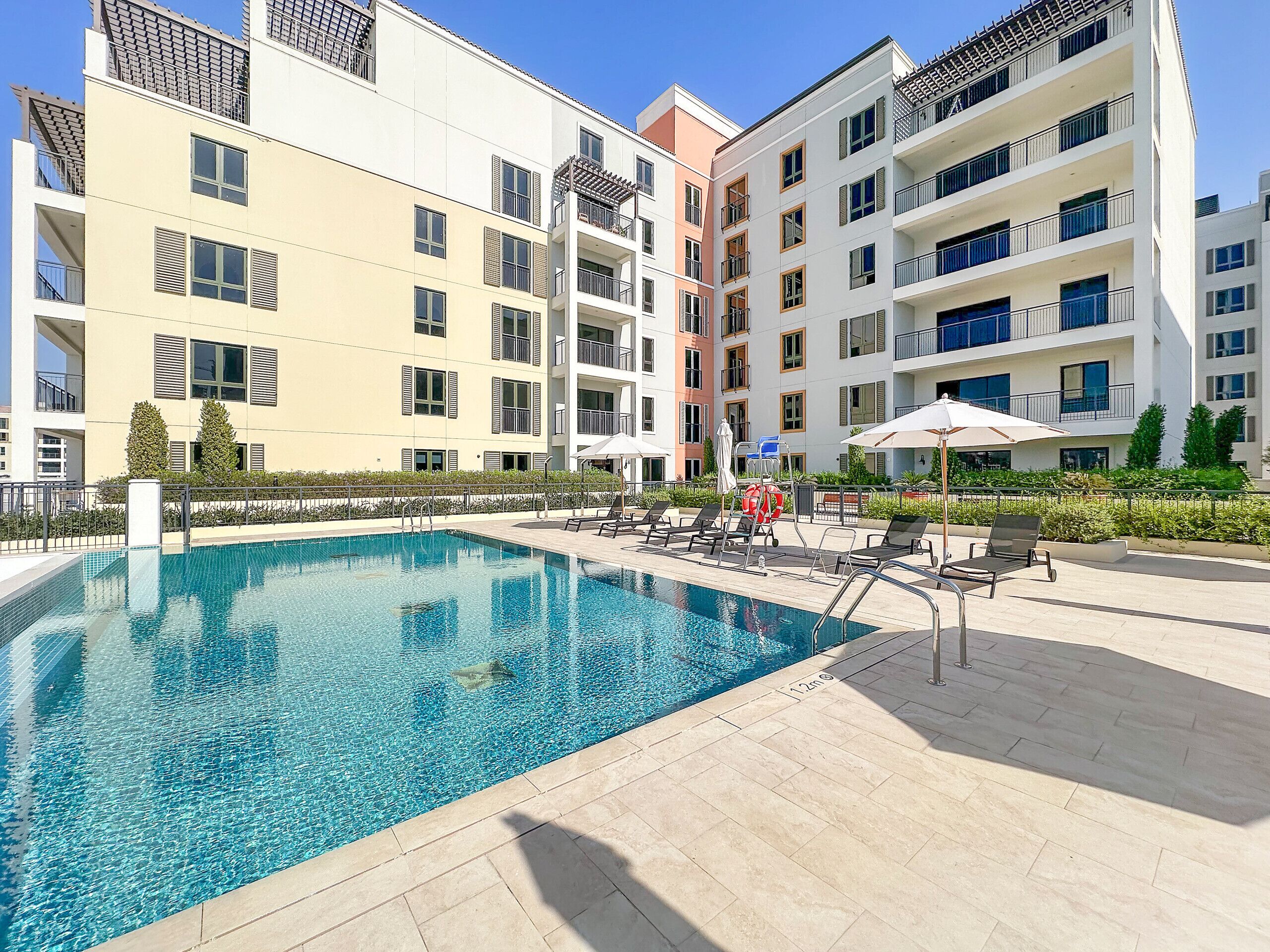 Une piscine entourée de bâtiments résidentiels à plusieurs étages dotés de balcons, avec des chaises longues et des parasols à proximité.