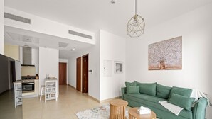 Ein modernes Wohnzimmer mit einem grünen Sofa, Holznachttischen und einer Küchenzeile mit Herd und Schränken.