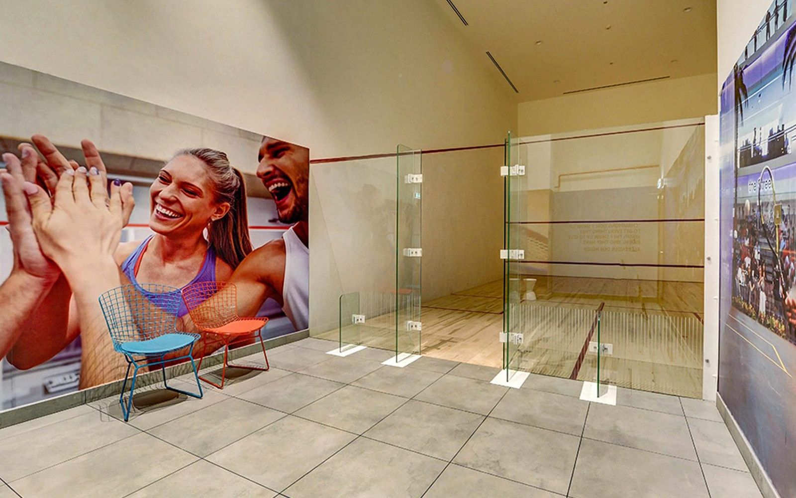 A squash court with glass walls, a tiled floor, and a poster of a sports event.