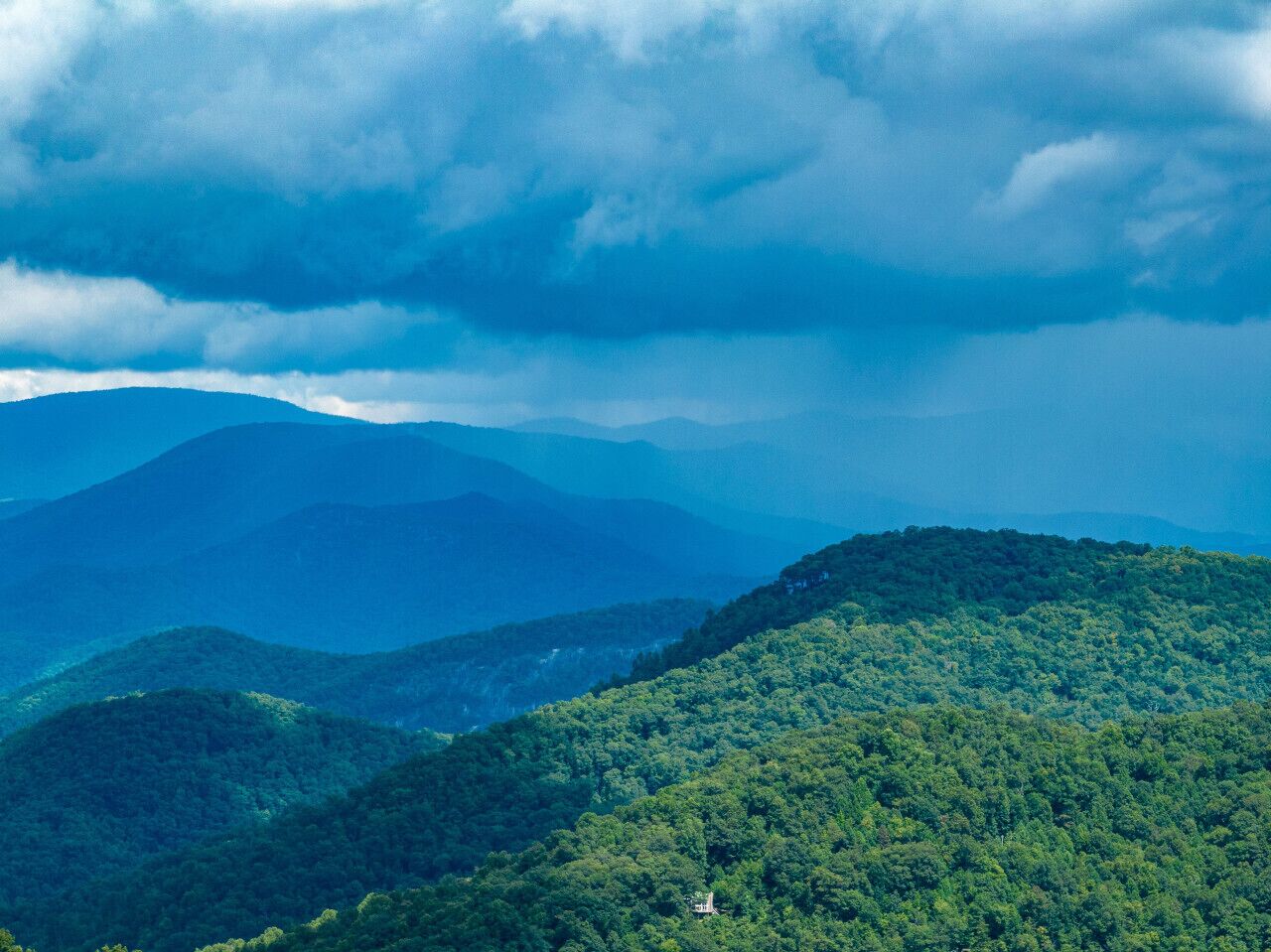 A mountainous landscape with dense forest coverage and a small structure on a hill.