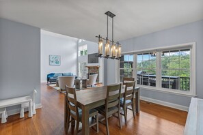 A dining area with a wooden table and chairs, a chandelier, and a large window with a view of greenery. - Lake access with mountain views! (Cullowhee)