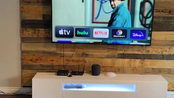 A flat-screen TV mounted on a wooden wall with a wooden cabinet below displaying various streaming services.