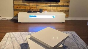 A modern living room with a flat-screen TV mounted on a wooden wall, a white entertainment unit below, and a geometric-patterned rug.