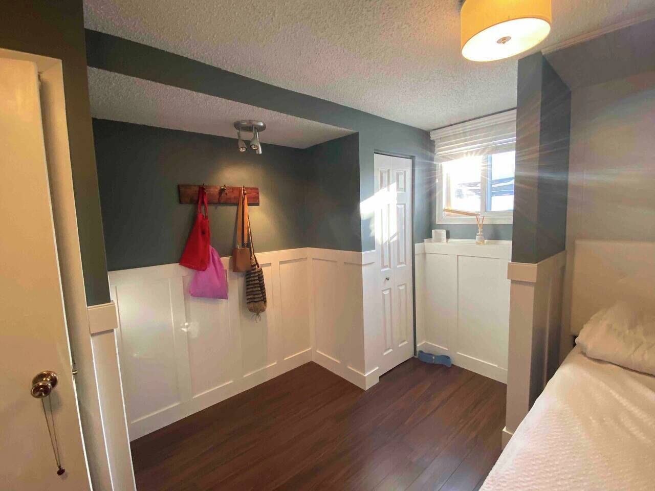 A bedroom with a bed, a door, a window, and a ceiling light.