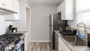 A modern kitchen with white cabinets, a stainless steel refrigerator, a gas stove, and a sink. - Cozy Euclid Home Near Lakefront (Euclid)