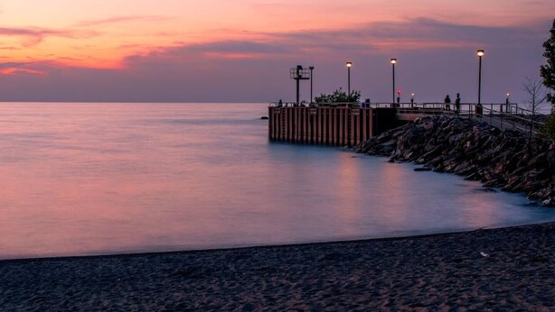 A pier extending into calm waters at dusk with a rocky shoreline. - Cozy Euclid Home Near Lakefront (Euclid)