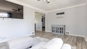 A spacious living room with a ceiling fan, a fireplace, and a large mirror on the wall. - Cozy Euclid Home Near Lakefront (Euclid)