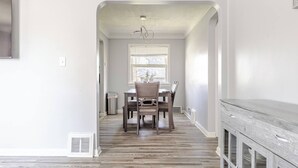A spacious hallway with a dining area featuring a wooden table and chairs, a window with blinds, and a built-in cabinet. - Cozy Euclid Home Near Lakefront (Euclid)