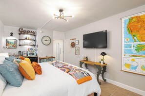 Un dormitorio con cama, televisión, un mapa en la pared y una kitchenette al fondo.