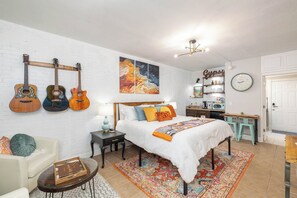 Un dormitorio con cama, mesita de noche, silla, escritorio y una pared decorada con guitarras y un cuadro.