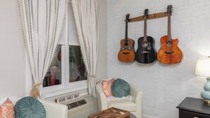 A living room with two white armchairs, a glass coffee table, and a wooden guitar wall hanging. - Gypsy Essence: Free Parking | Steps to Downtown (Eureka Springs)