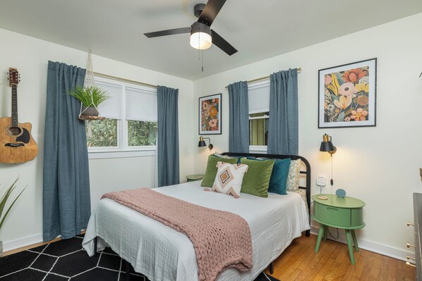 A bedroom with a bed, a guitar, a plant, and artwork on the walls.
