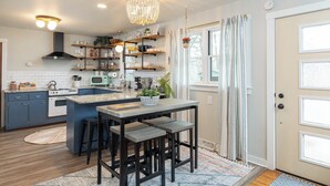 A modern kitchen with a central island, bar stools, and a chandelier.