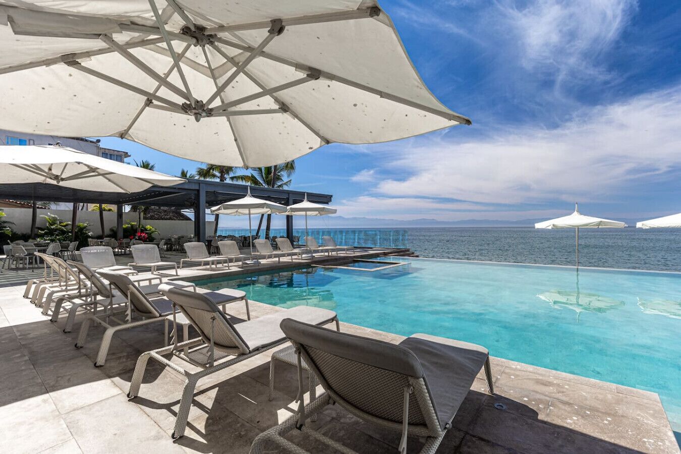 An infinity pool with lounge chairs and umbrellas, overlooking the sea.