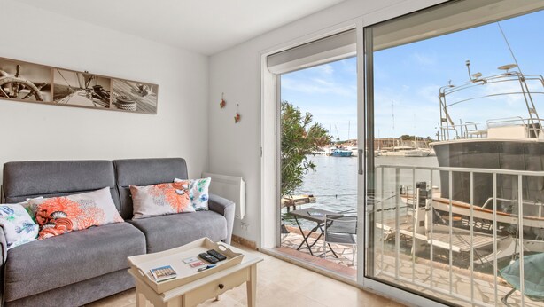 A balcony with a view of boats, a grey sofa with colorful cushions, and a small table with a tray. - Very pleasant ground-floor apartment near the beach (Grimaud)