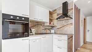 A modern kitchen with white cabinetry, a built-in oven, and a marble backsplash. - Very pleasant ground-floor apartment near the beach (Grimaud)