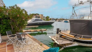 A marina with boats docked, a small outdoor seating area with chairs and a table, and a stone-paved dock. - Very pleasant ground-floor apartment near the beach (Grimaud)