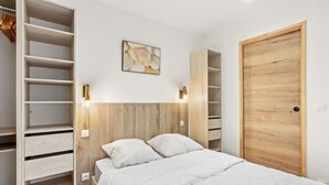 A bedroom with a bed, wooden headboard, built-in shelving, and a wooden door. - Very pleasant ground-floor apartment near the beach (Grimaud)
