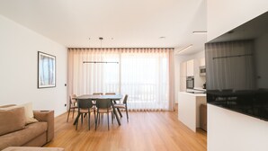 A modern living room with a sofa, dining table, and chairs, a kitchen area with a TV, and large windows with curtains. - Apartment 'Maso Renner 8' with Mountain View, Wi-Fi and Air Conditioning (Laives)