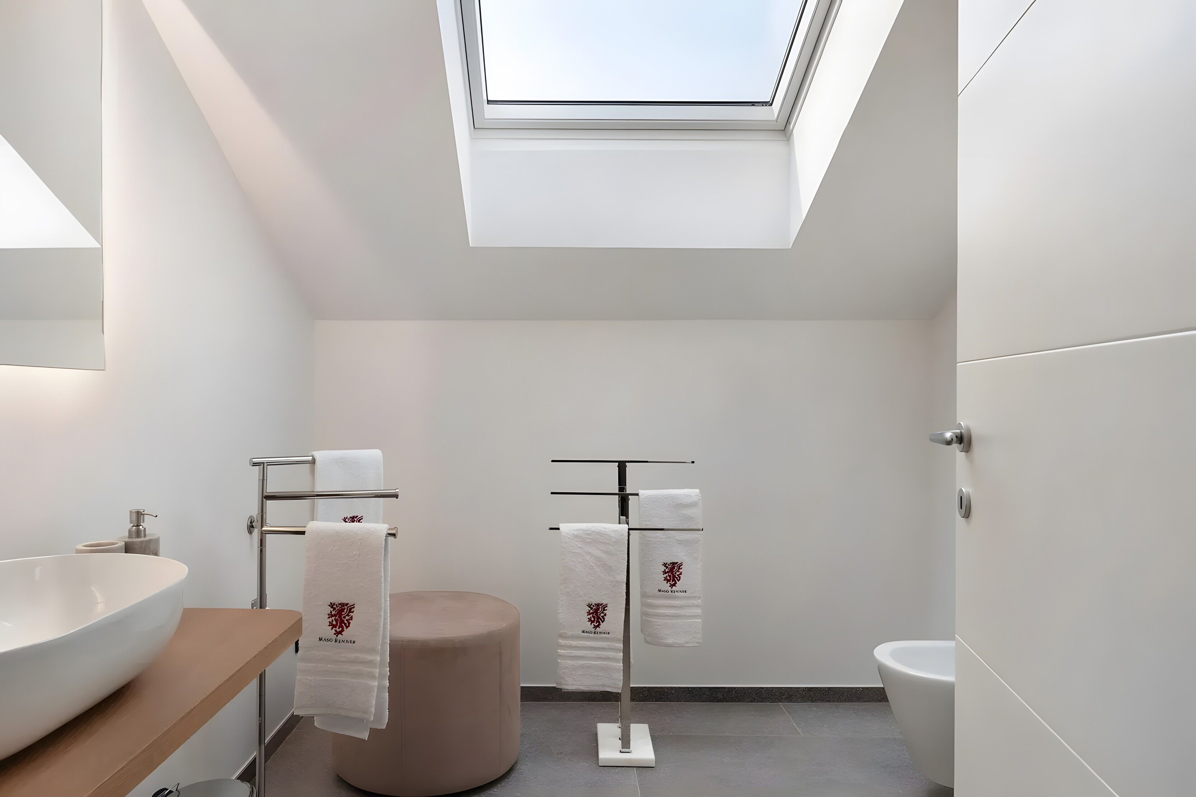 Une salle de bain moderne dotée d’un puits de lumière, d’un grand lavabo, de toilettes et d’un porte-serviettes.