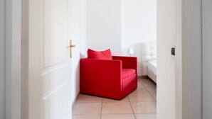 Un pasillo estrecho que conduce a una habitación con un sofá rojo y una cama blanca.