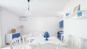 Una zona de dinar blanca amb una taula i cadires, un objecte decoratiu blau sobre la taula, un armari blanc amb portes blaves i un armari blau al fons.