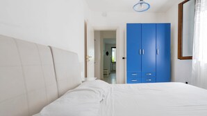 Un dormitori amb un llit, un armari blau i una porta que dona a una altra habitació.