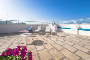 A rooftop terrace with white lounge chairs, a small table with glasses, and a railing. - Room 'Case Vacanze Otranto -  11' with Shared Terrace, Wi-Fi and Air Conditioning (Otranto)