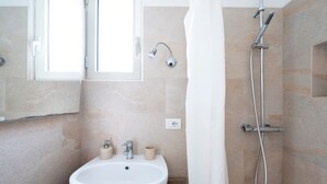 A bathroom with a white sink, a shower with a handheld showerhead, and a window.