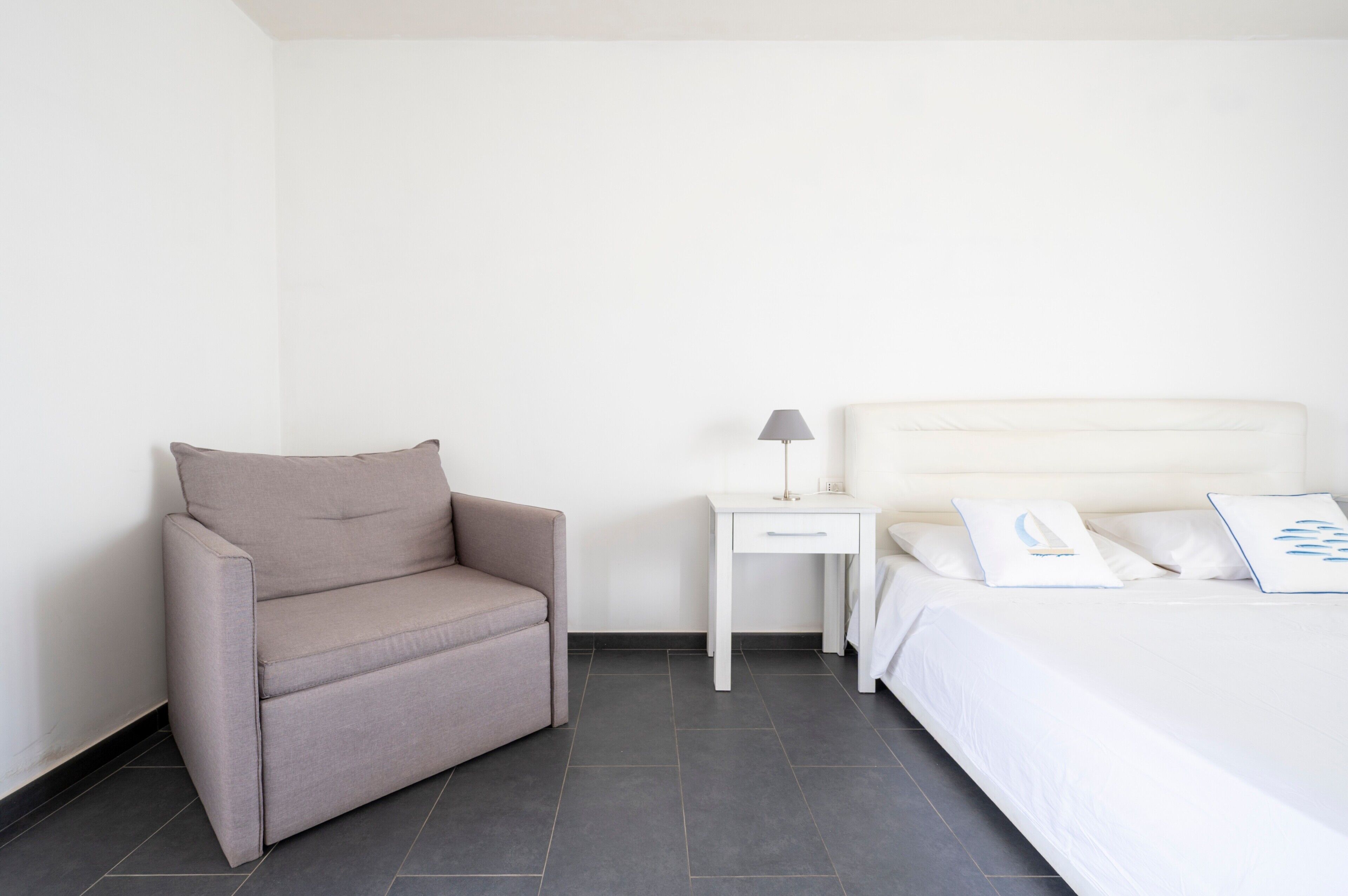 Een minimalistisch hotelkamer met een bank, een nachtkastje met lamp en een bed met wit beddengoed.