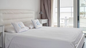 A modern hotel room with a large bed, a nightstand, a lamp, and a view of the outside.