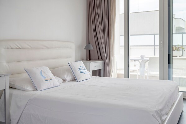 A modern hotel room with a large bed, a nightstand, a lamp, and a view of the outside.