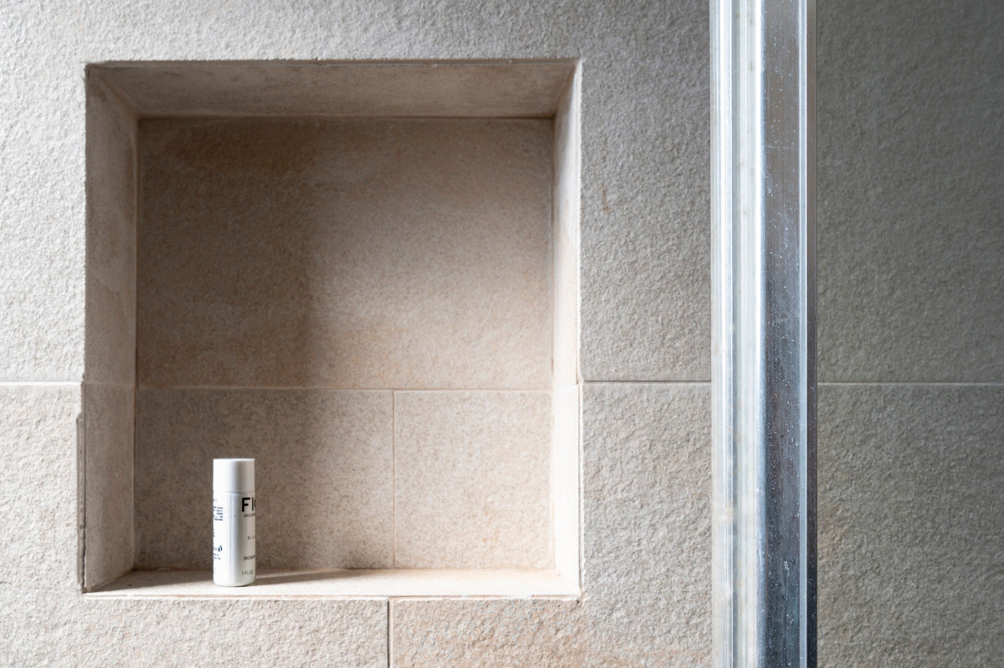 A bathroom with a tiled wall, a small shelf, and a bottle.