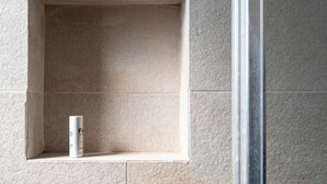 Un baño con pared de azulejos, un estante pequeño y una botella.