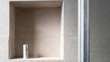 A bathroom with a tiled wall, a small shelf, and a bottle.