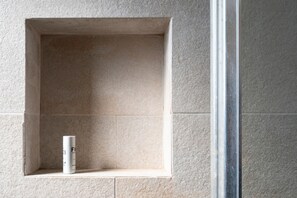 Une salle de bain avec un mur carrelé, une petite étagère et une bouteille.