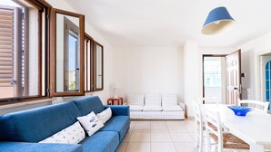 Un salon avec un canapé bleu, un canapé blanc, une table à manger et un luminaire suspendu bleu.