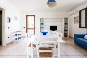 Een eetgedeelte met een witte tafel, stoelen, een blauwe kom en een televisie aan een witte muur.