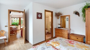 Une chambre à coucher avec un lit, une commode en bois et un miroir. Une porte donne accès à une salle de bain et à un coin repas.