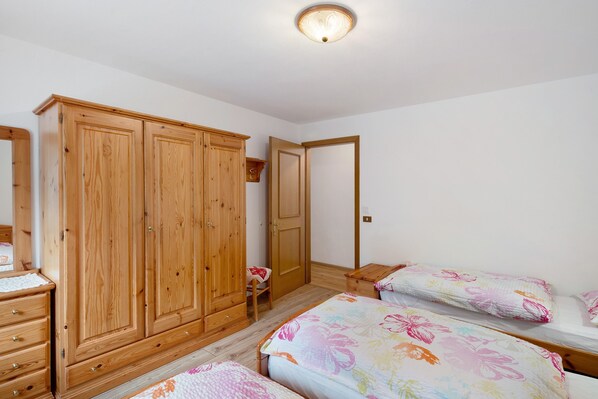Un dormitorio con armarios de madera, una cama con ropa de cama floral, una mesita de noche y una pequeña silla.