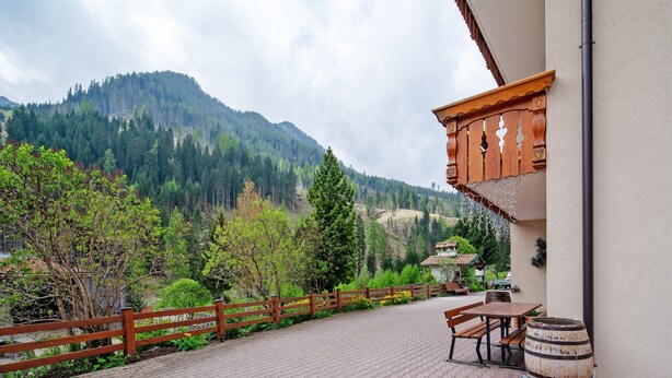 Une terrasse dallée, agrémentée de meubles en bois, d’un tonneau et offrant une vue sur une montagne.