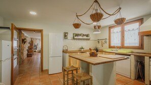 A kitchen with a central island, wooden stools, hanging baskets, and a view into the dining area. - Holiday Home 'La Alameda' with Private Pool, Garden, BBQ & Wi-Fi (MARAZUELA)