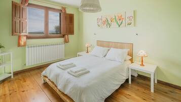 Un dormitorio con cama, mesitas de noche, una ventana con cortinas, un radiador y una pared decorada con motivos florales.