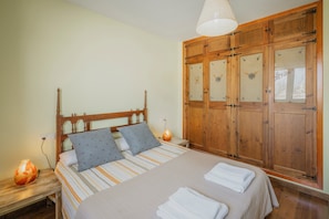 Une chambre à coucher avec un lit en bois, deux tables de chevet, une commode, une armoire et un luminaire suspendu.