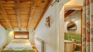 A bedroom with a wooden ceiling, a window, a radiator, a bed with a green bedspread, and a bathroom with a sink and mirror. - Holiday Home 'La Alameda' with Private Pool, Garden, BBQ & Wi-Fi (MARAZUELA)