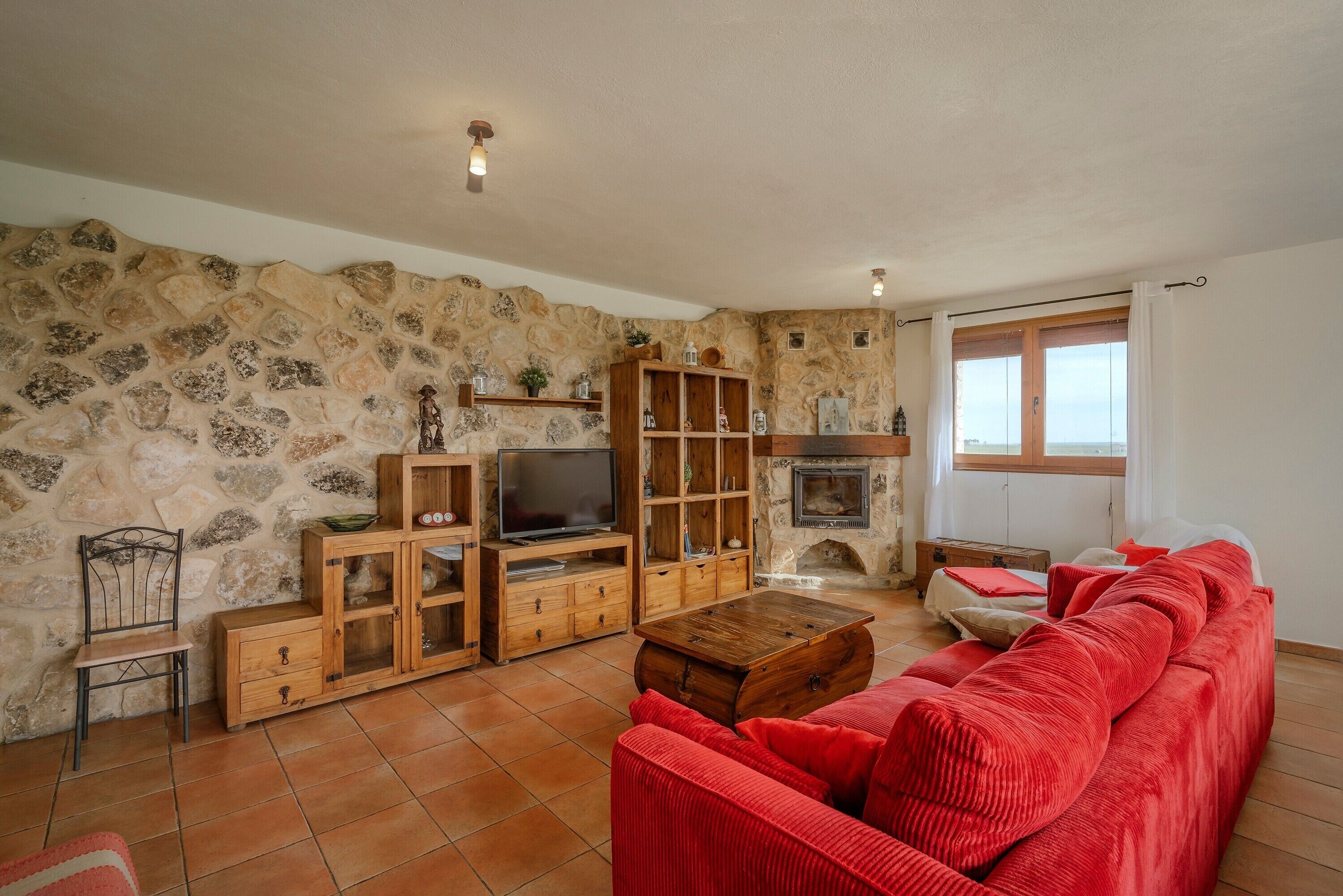 Una sala de estar con paredes de piedra, un mueble de madera para entretenimiento, un sofá rojo y una chimenea.