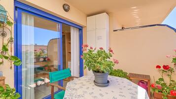 Un pequeño patio con una mesa, sillas, una planta en maceta y un ventanal corredero que da a una habitación.