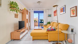 A living room with a sofa, TV, wooden cabinet, and a balcony with plants. - Apartment 'Argia' with Sea View, Wi-Fi, and Air Conditioning (Algarrobo)